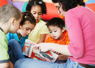 a group of children being read a book by an adult child care taker