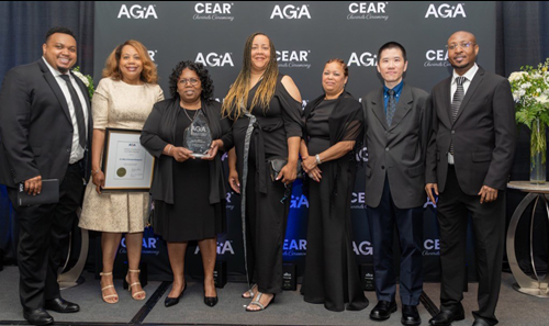 OPM OCFO staff stand on stage to receive the AGA Certificate of Excellence in Accountability Reporting award. One staff member holds the award, while another holds the framed certificate.